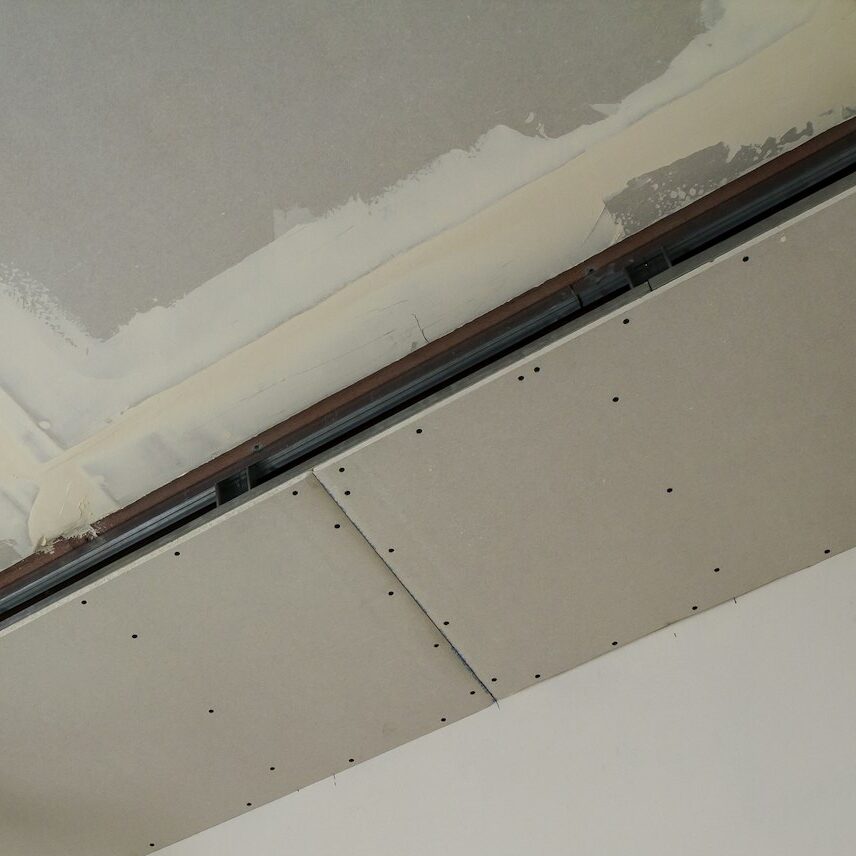 Construction worker assemble a suspended ceiling with drywall and fixing the drywall to the ceiling